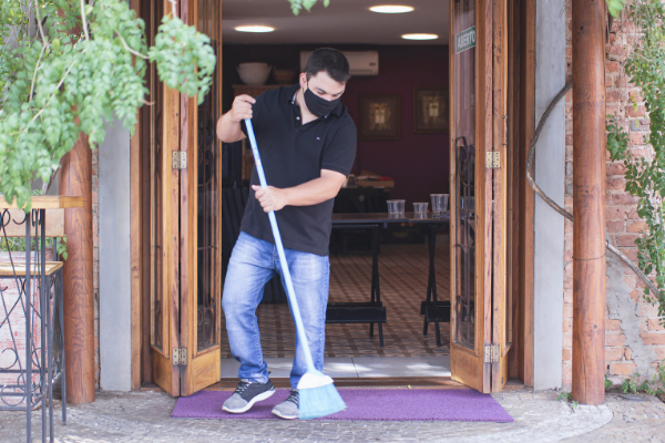 Man sweeping front doorstep with a facemask on