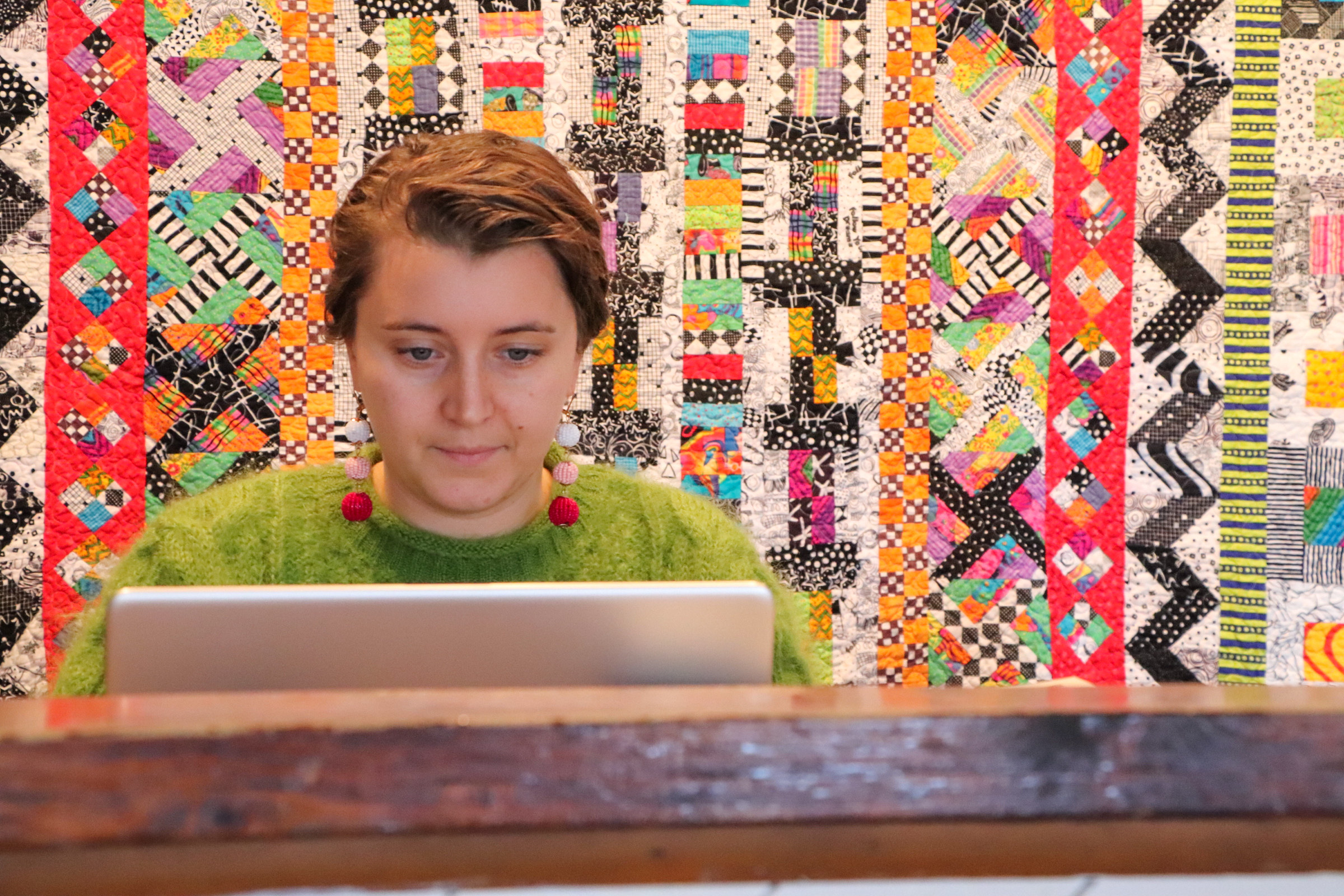 Woman working on computer with patterned quilt behind her