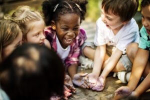 Kids sitting in a circle with their hands in the center of them on the ground with their palms up