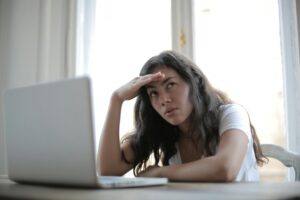 A weary entrepreneur sitting at a cluttered desk, with a laptop. The entrepreneur a hand on their head, looking tired and overwhelmed, but with a determined look in their eyes.
